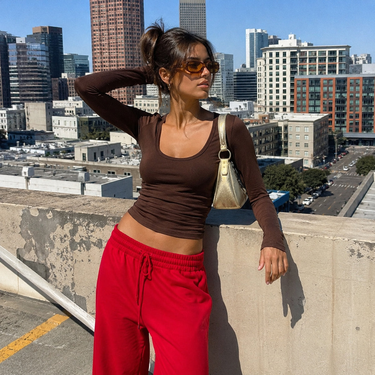 Woman in a brown top and red trousers on a car park deck in front of the skyline